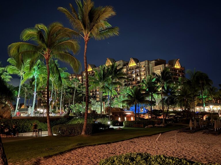 Aulani's towers lit at night behind palms on the beach