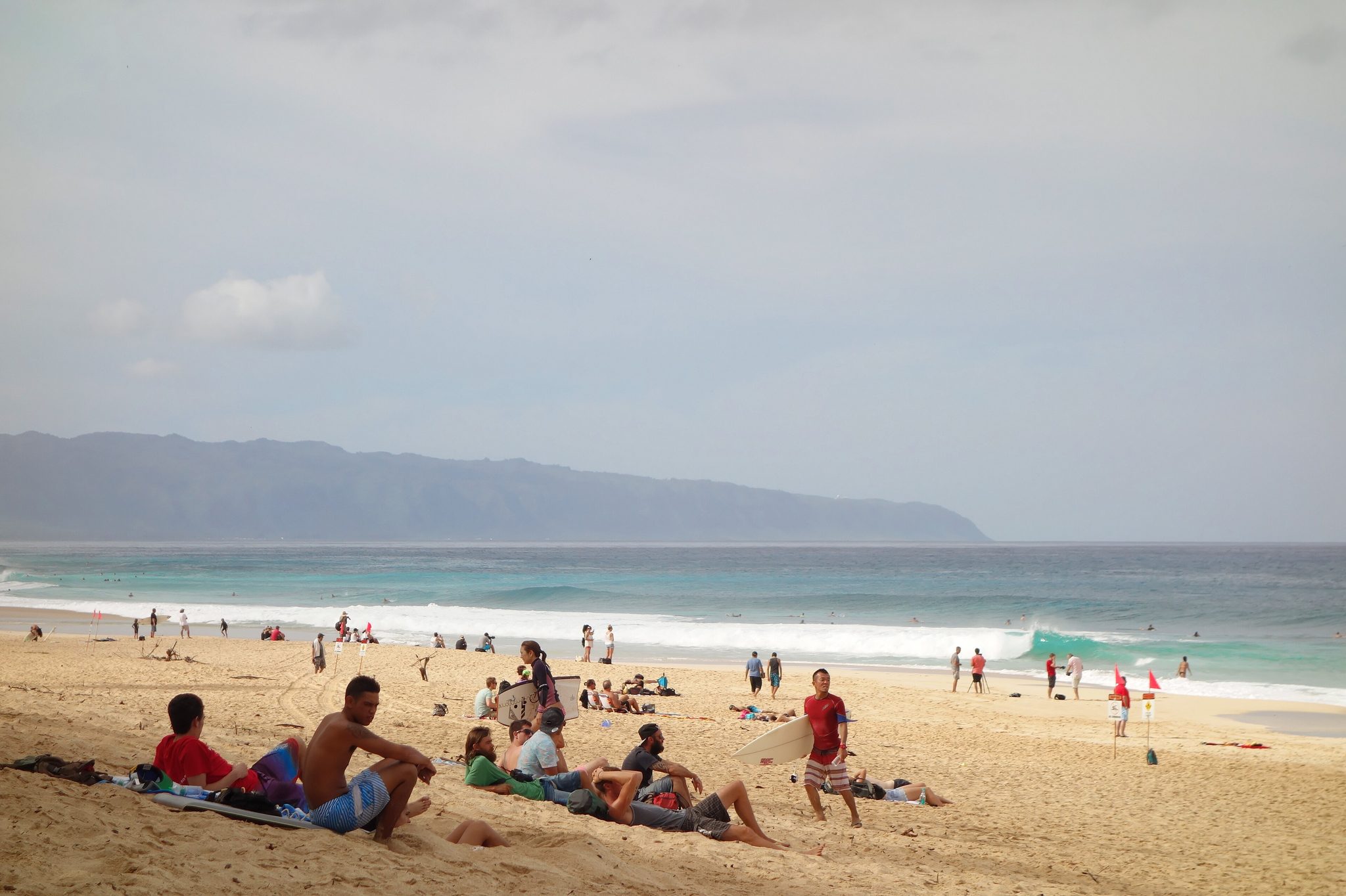Spectators on the sand at Ehukai Beach watching waves break at the Banzai Pipeline on Oahu's North Shore