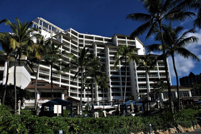 The Four Seasons Oahu tower through palms above poolside cabanas