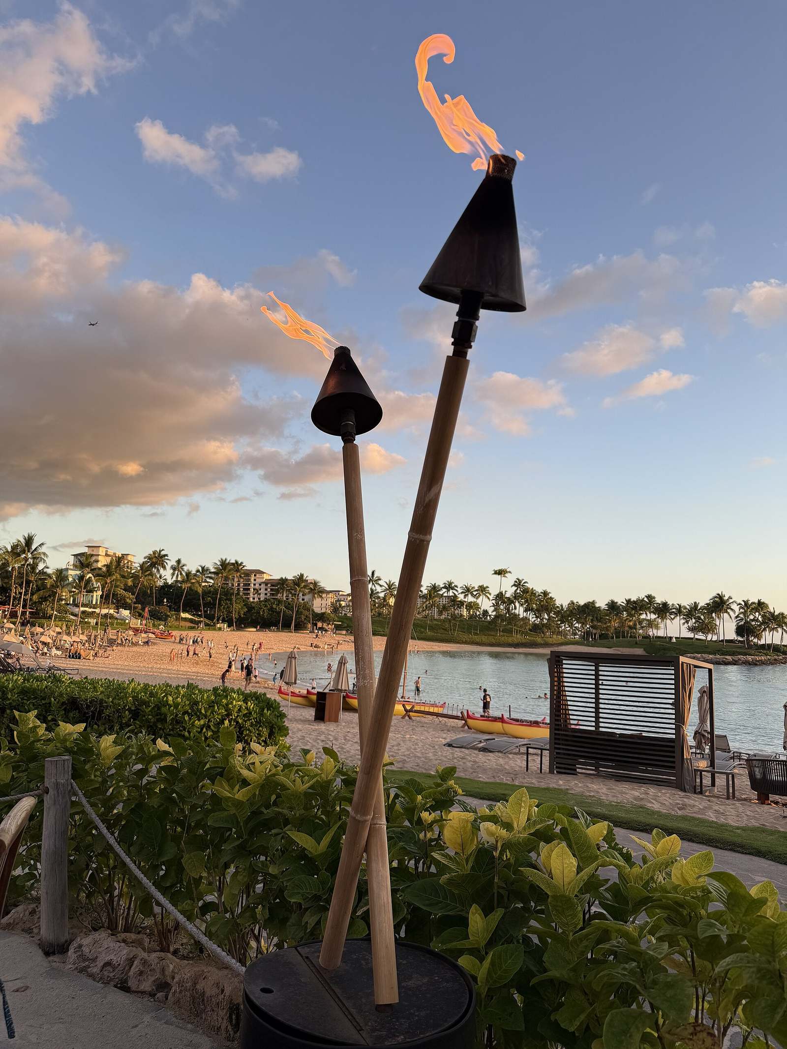 Tiki torches at golden hour over a Ko Olina lagoon beach, with outrigger canoes on the sand