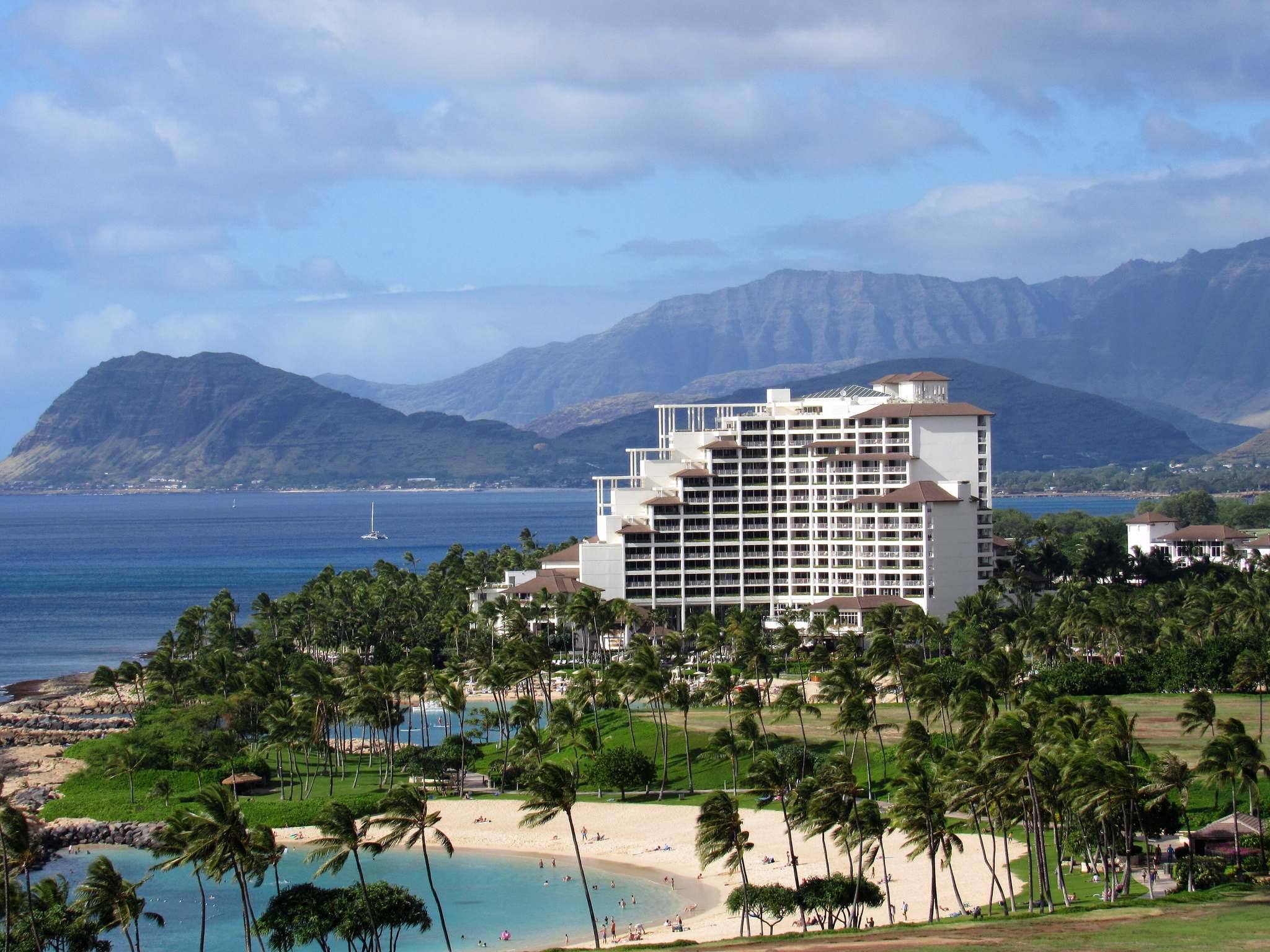 The Four Seasons Oahu tower above a Ko Olina lagoon beach and palms, with the Waianae Mountains behind