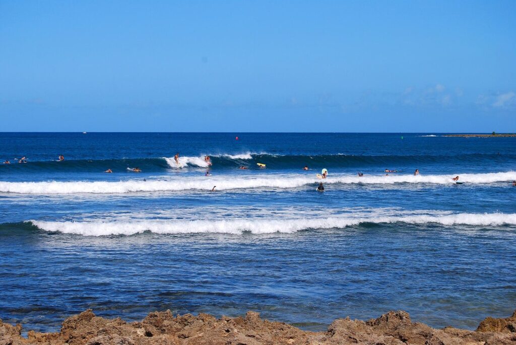 Surfers and bodyboarders on lines of breaking waves off a rocky shoreline at Haleiwa on Oahu's North Shore