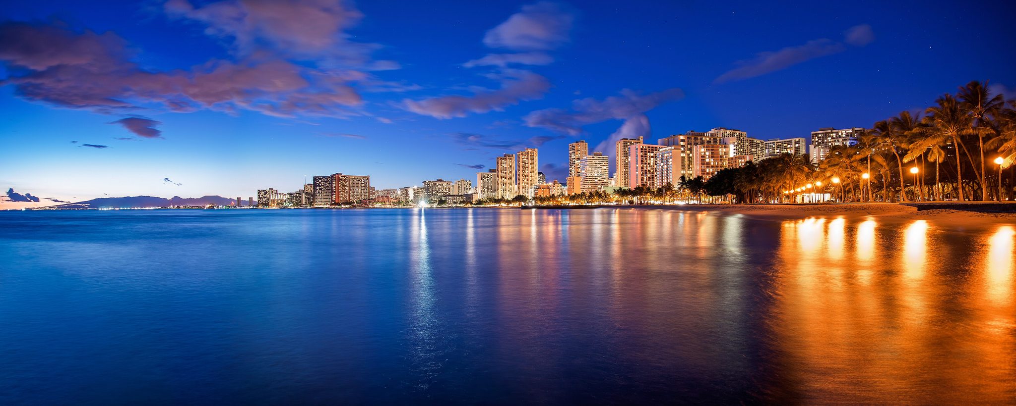 Waikiki Beach and its hotel towers lit up at dusk, seen from Sans Souci Beach