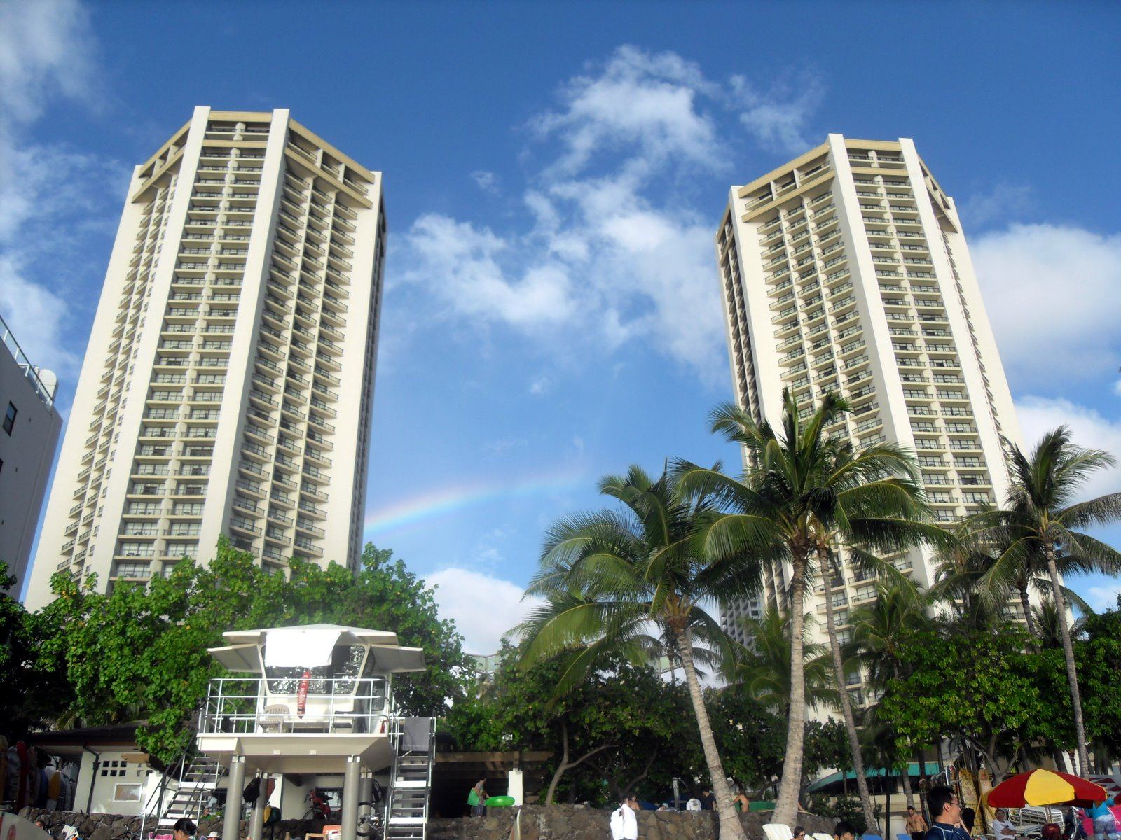 The twin towers of the Hyatt Regency Waikiki behind a Kuhio Beach lifeguard tower, with a rainbow