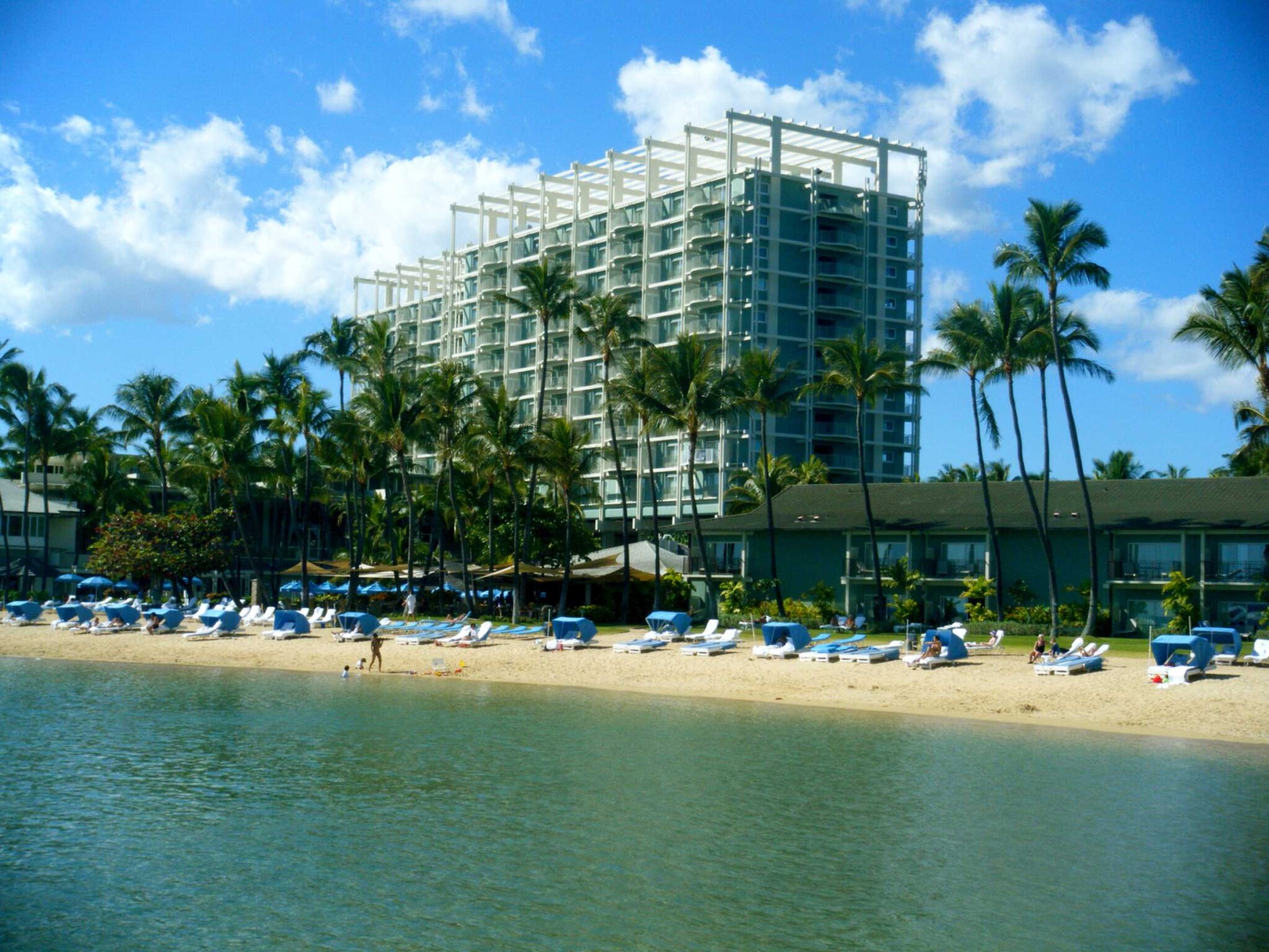 The Kahala Hotel tower above its beach, palms and lounge chairs