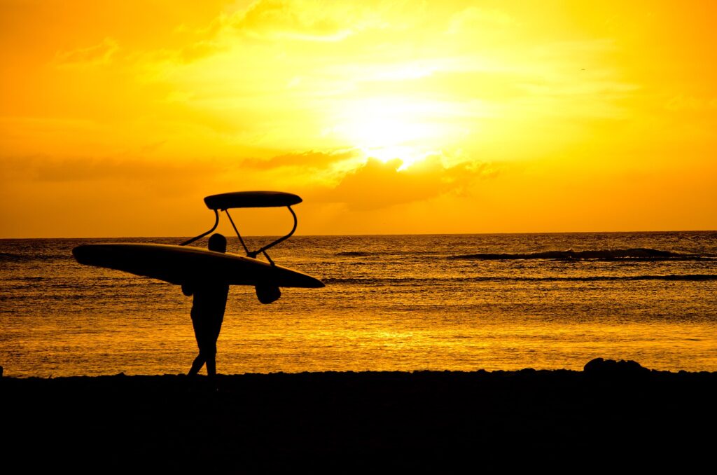 A surfer carries a board along Kaimana Beach at sunset, at the Diamond Head end of Waikiki