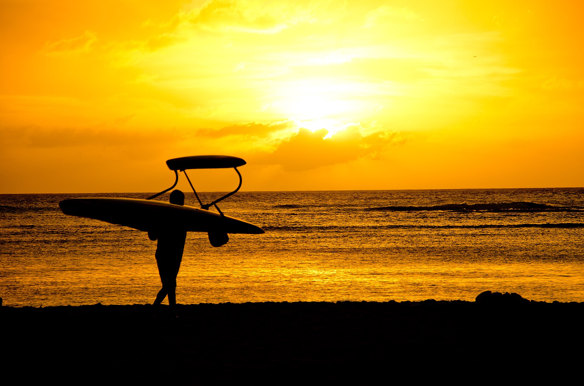A surfer carries a board along Kaimana Beach at sunset, at the Diamond Head end of Waikiki