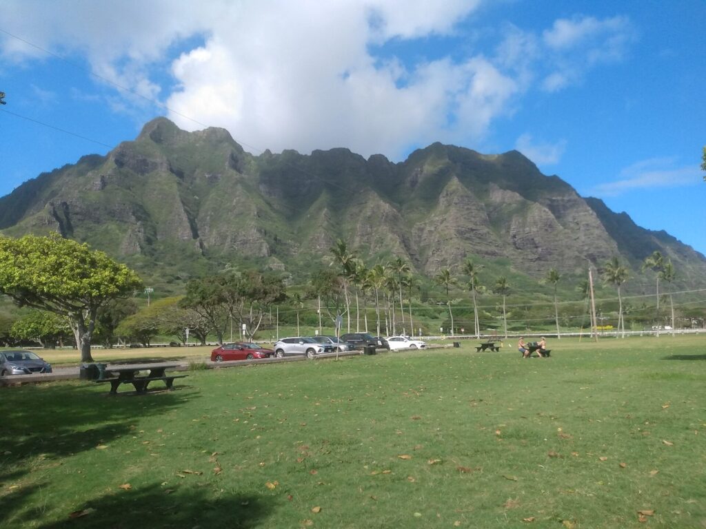 The grassy lawn and picnic tables of Kualoa Regional Park on Oahu, below a steep green mountain ridge