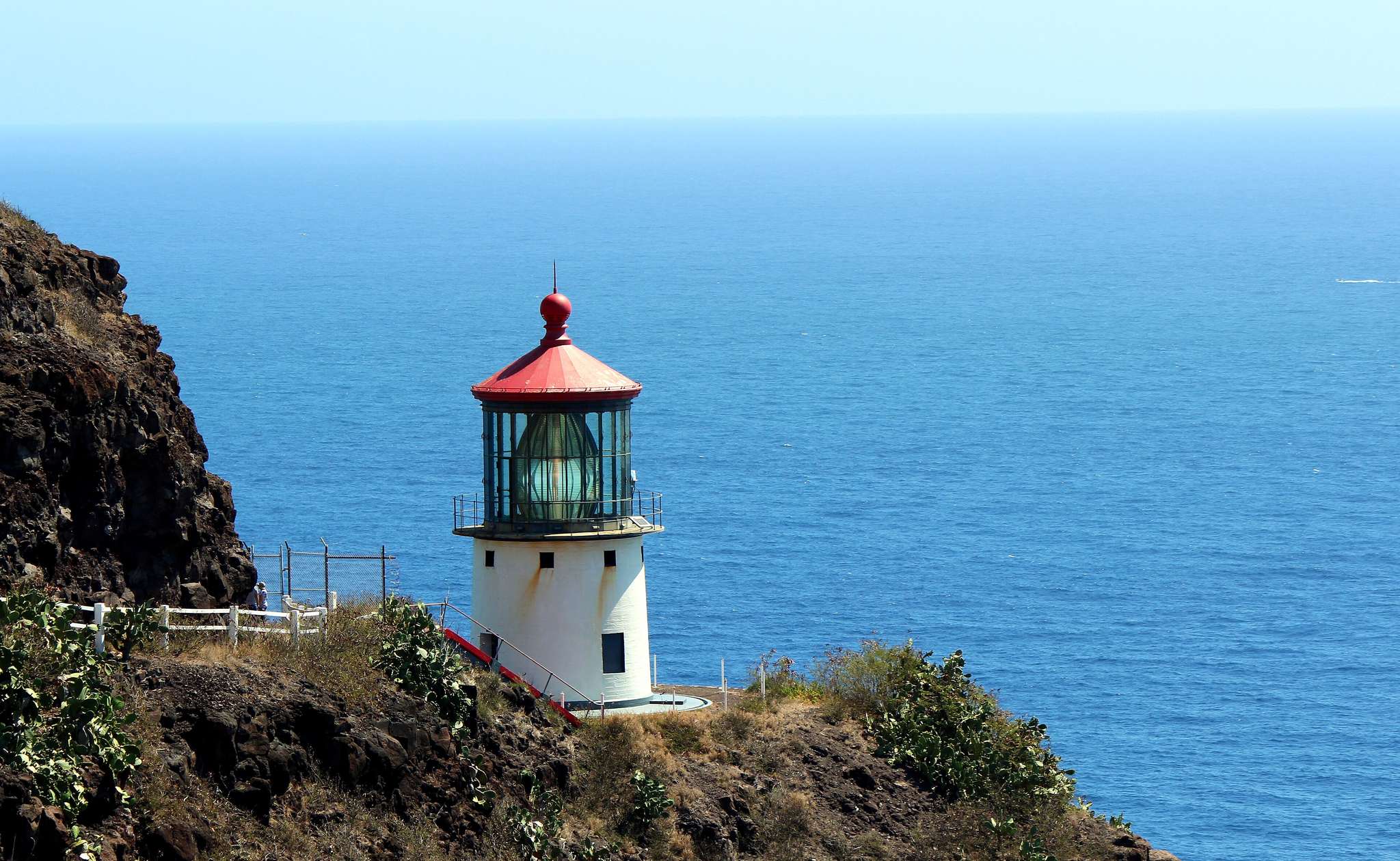 The red-roofed Makapuu Point Lighthouse on a cliff above the ocean, the far point of the east side Oahu drive