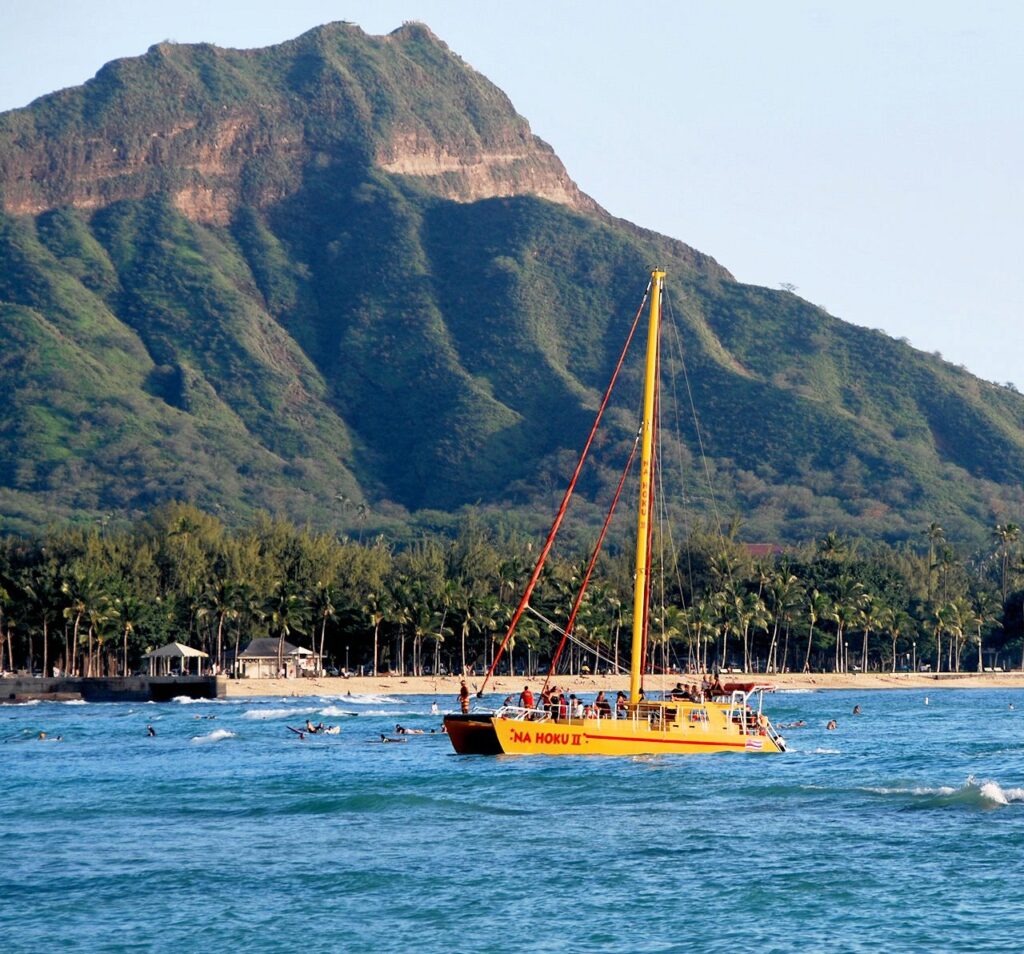 The yellow Na Hoku II catamaran under sail off Waikiki, with Diamond Head behind