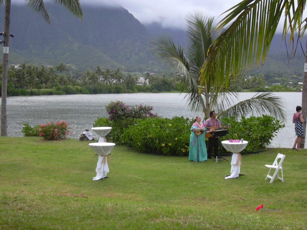 Musicians with ukulele and guitar playing on a lawn beside a fishpond at a wedding reception in Kahaluu, Oahu
