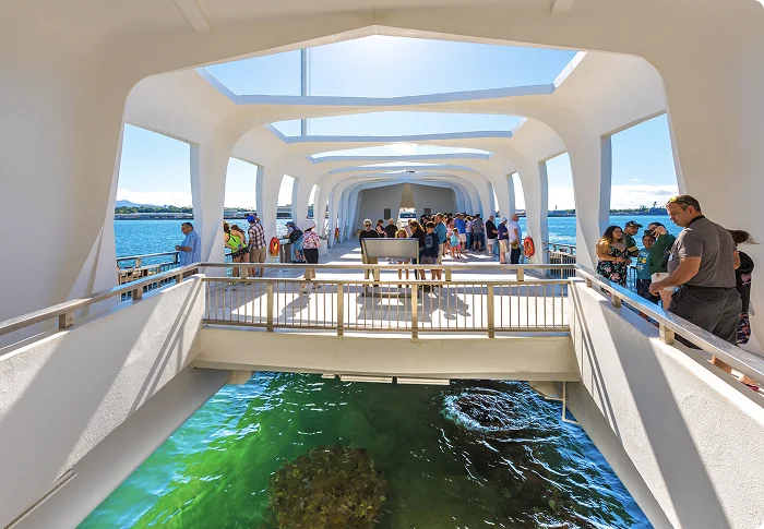 Visitors inside the USS Arizona Memorial at Pearl Harbor, standing on the open deck above the sunken battleship