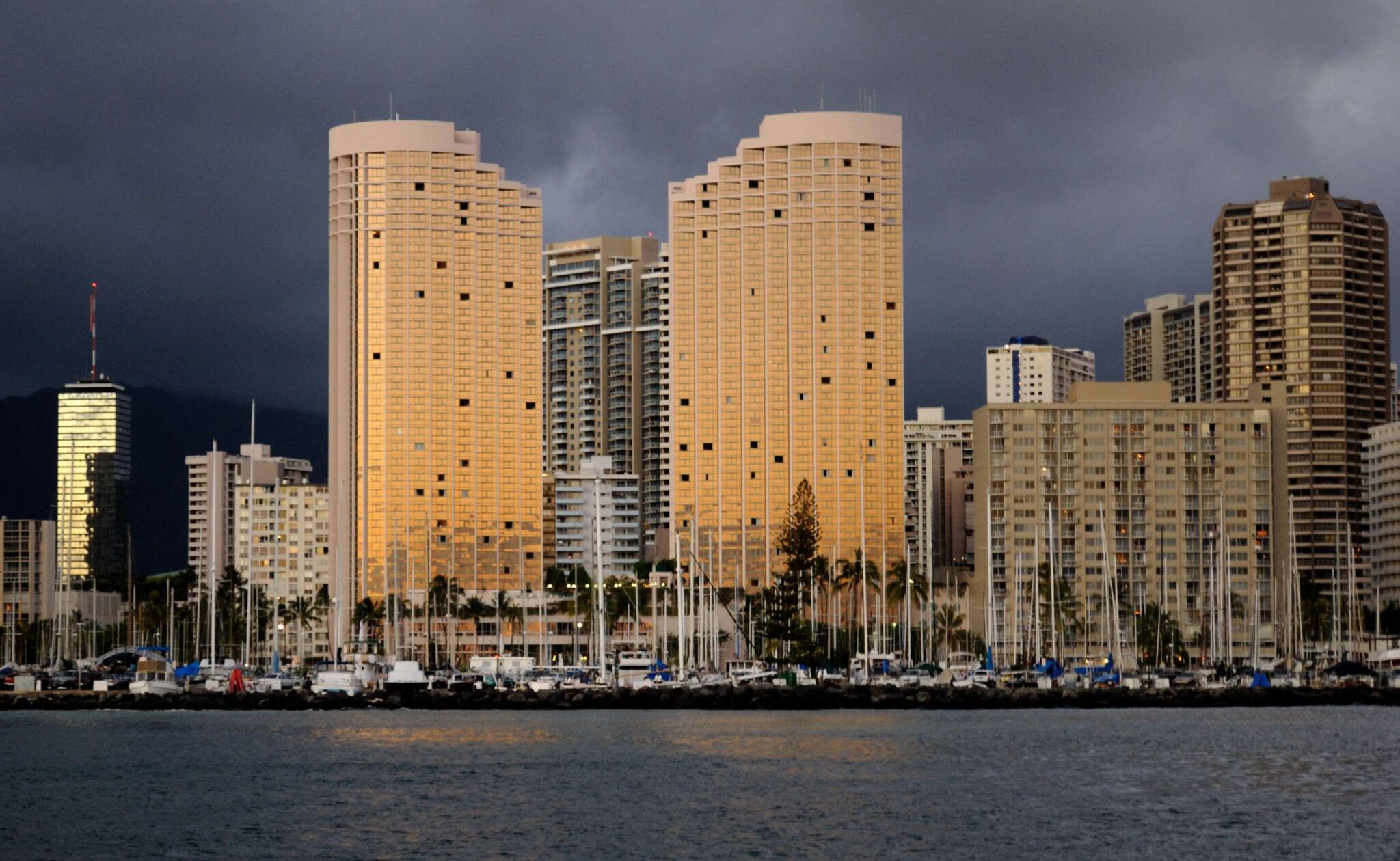 The Prince Waikiki towers lit at sunset over the boats of the Ala Wai Boat Harbor
