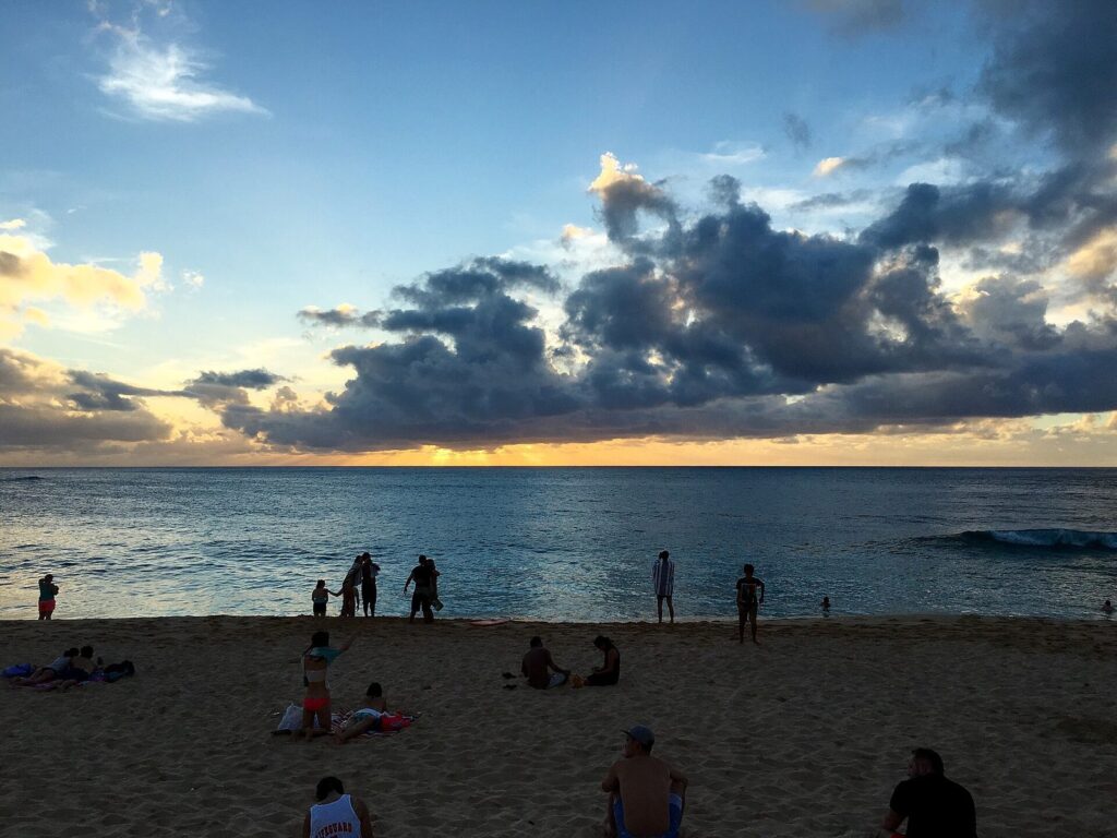 People on the sand at Sunset Beach on Oahu's North Shore as the sun goes down behind clouds