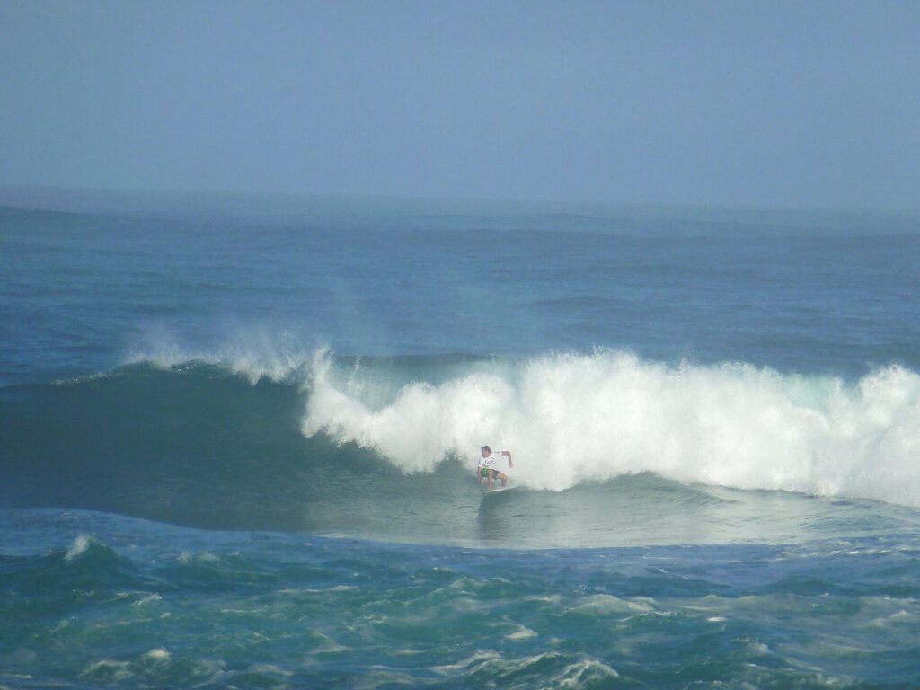 A surfer riding a winter wave at Sunset Beach on Oahu's North Shore as whitewater breaks behind him