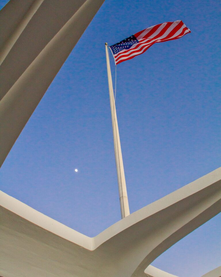 The American flag flying above the open roof of the USS Arizona Memorial at Pearl Harbor
