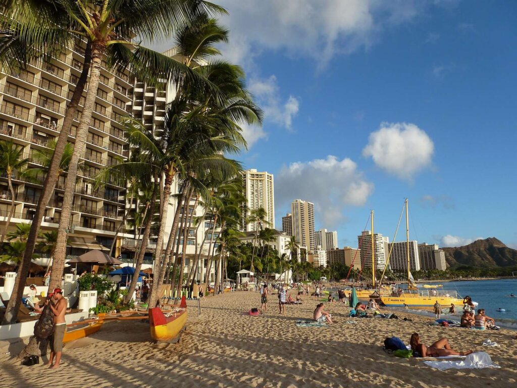 A yellow catamaran pulled up on the sand at Waikiki Beach, with palms, hotels and Diamond Head behind