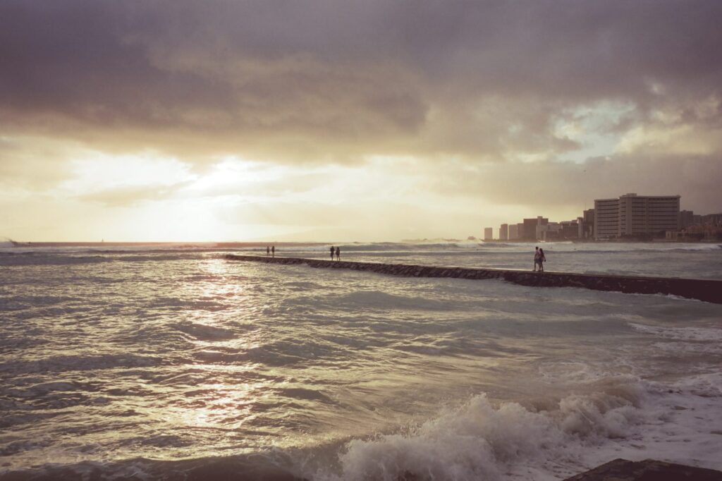 People walking out on a Waikiki breakwall at sunset under a cloudy sky