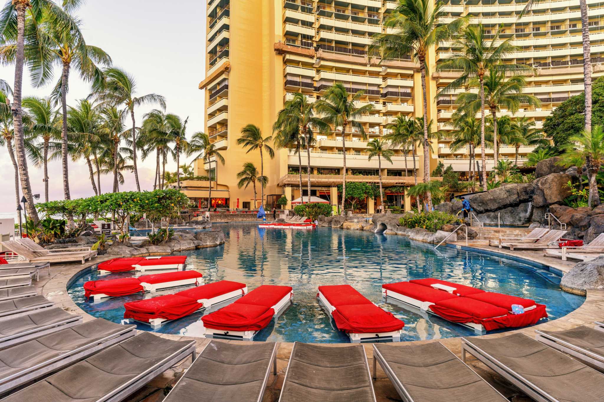 Red loungers floating in a pool at the Sheraton Waikiki, with palms and the hotel tower behind
