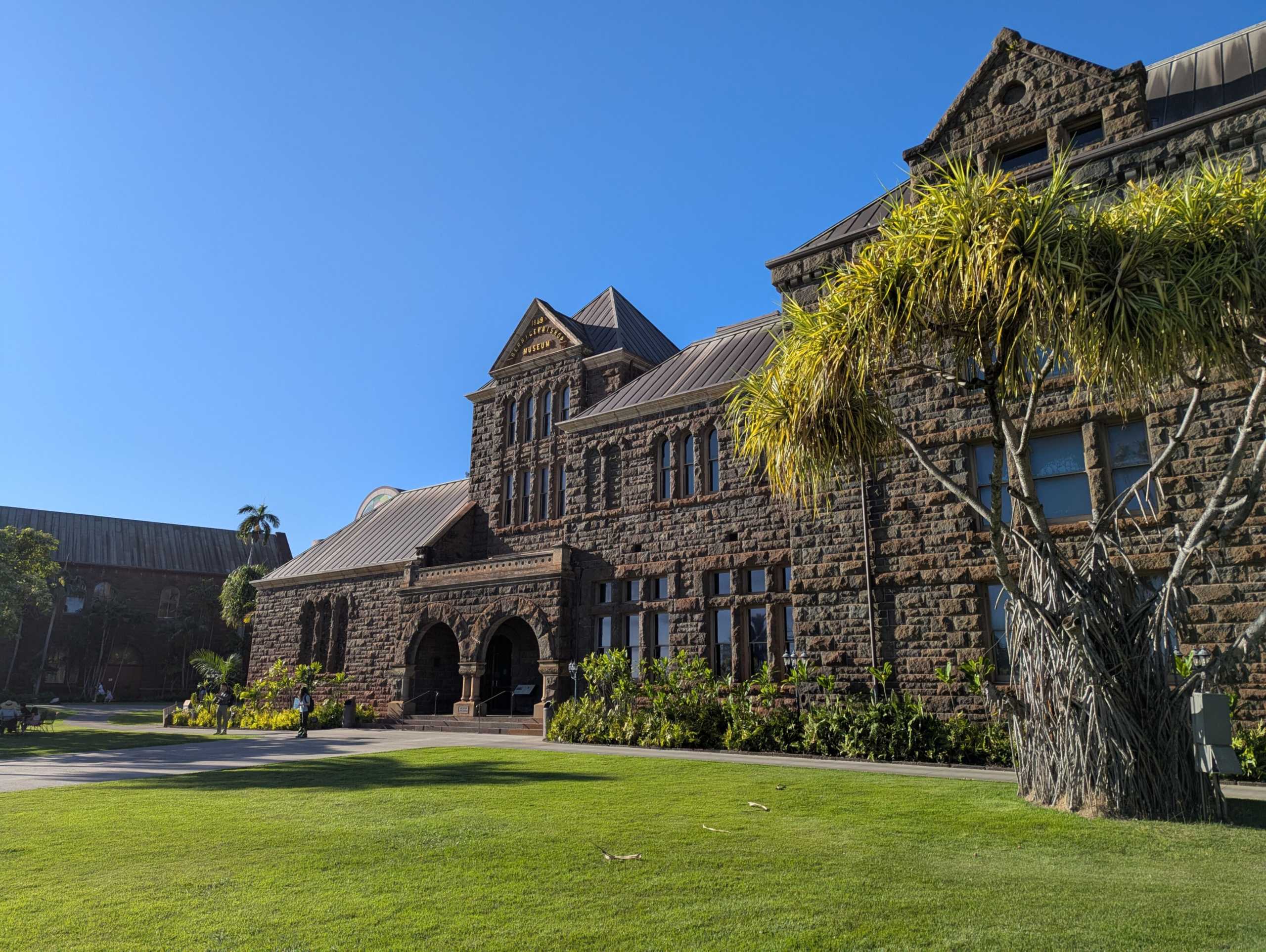 The stone facade of Bishop Museum’s Hawaiian Hall in Honolulu behind a lawn