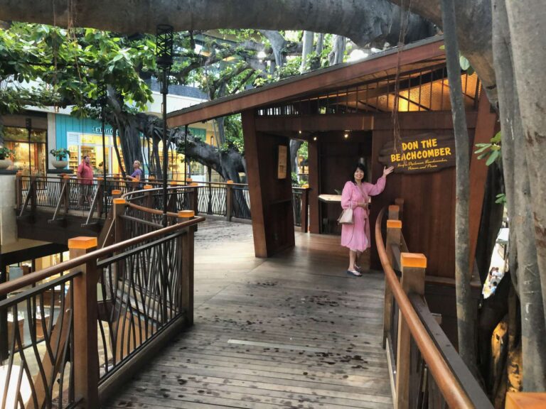 A woman stands at the Don the Beachcomber treehouse on a wooden walkway among the banyan branches