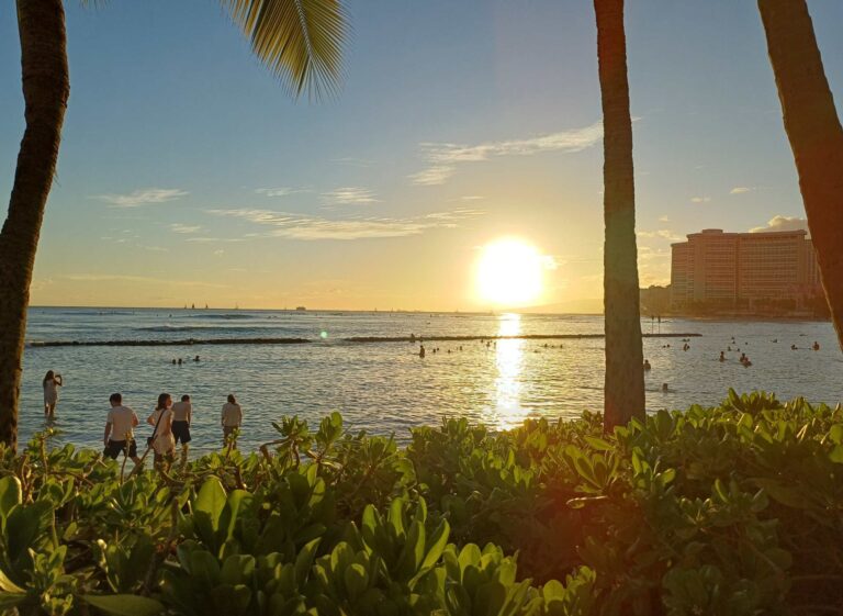 The sun setting over the Kūhiō Beach swim basin with the Waikīkī hotel row on the right