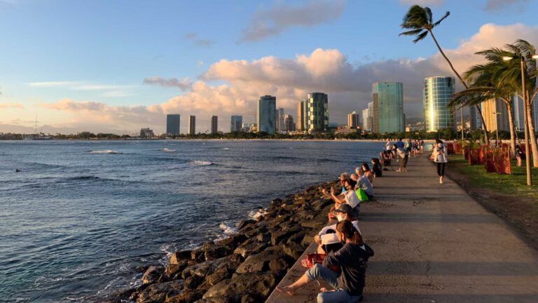 People sitting on the rocks along the Magic Island path to watch the sunset, with the Ala Moana skyline behind