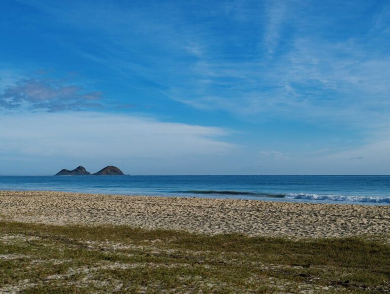 Nā Mokulua islets seen across Waimanalo Bay from the sand at Bellows, with a small wave breaking on the shore