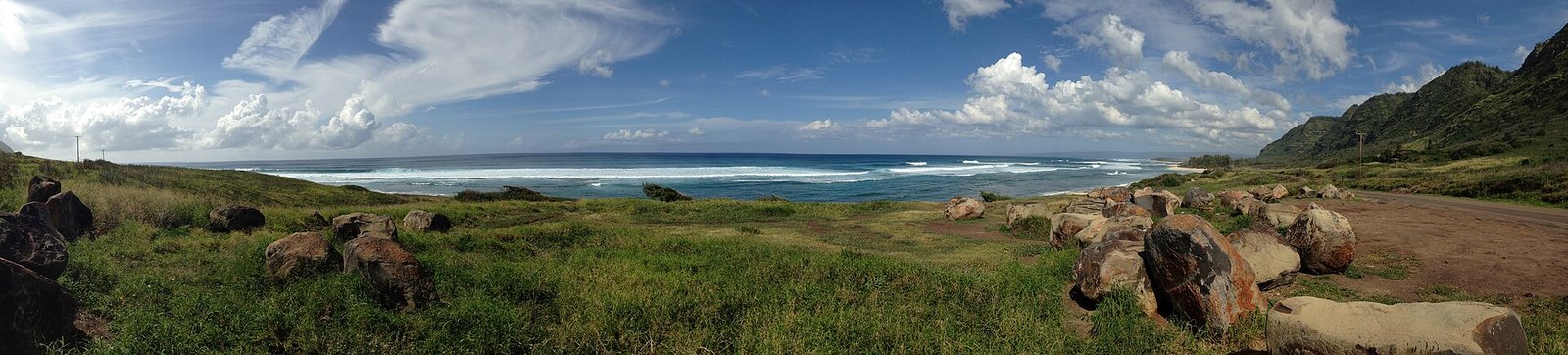 Surf, grass and boulders at the Kaʻena Point Mokulēʻia trailhead with the Waiʻanae range at right