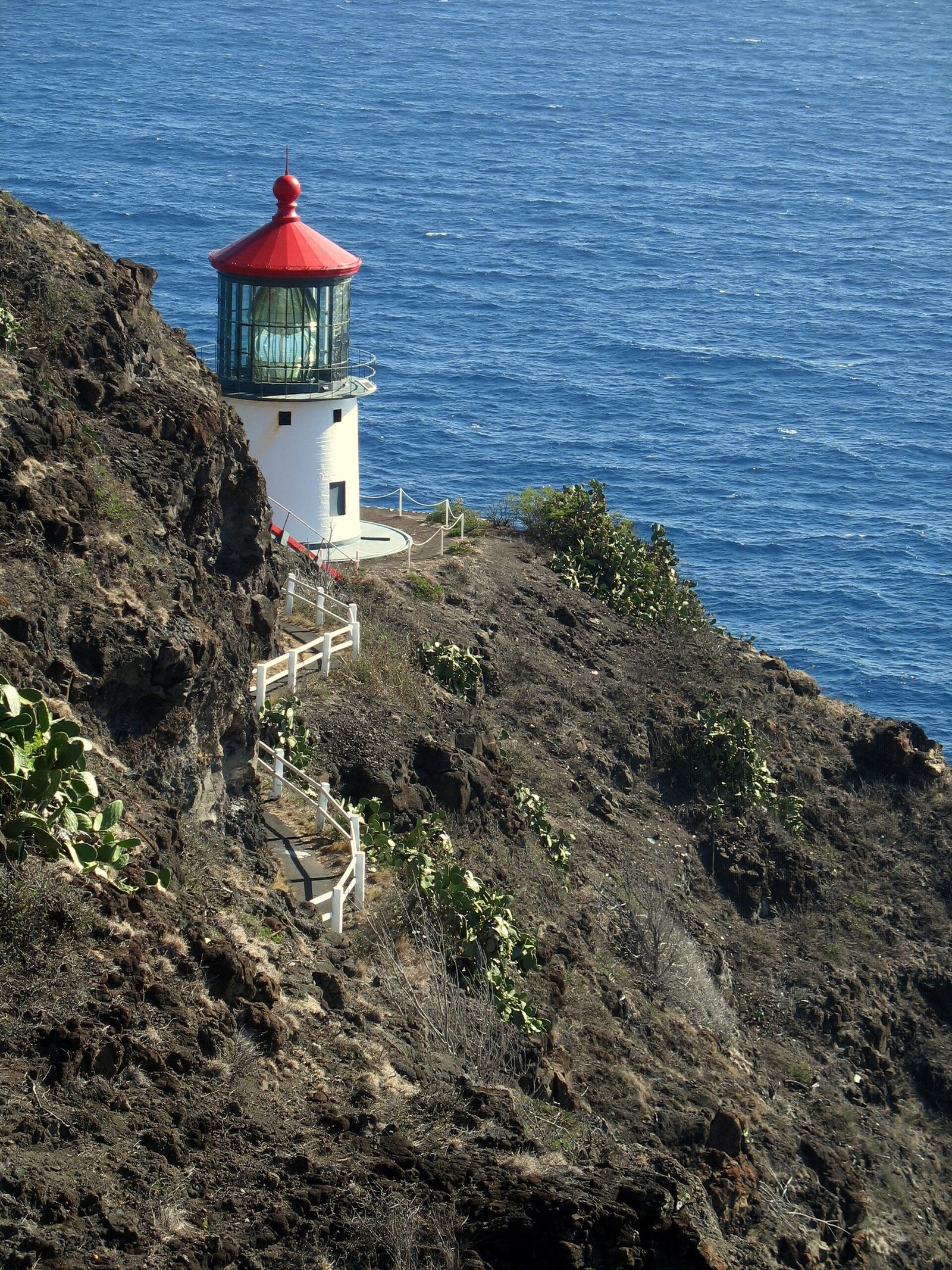 The red-roofed Makapuʻu lighthouse and its railed path seen from the trail