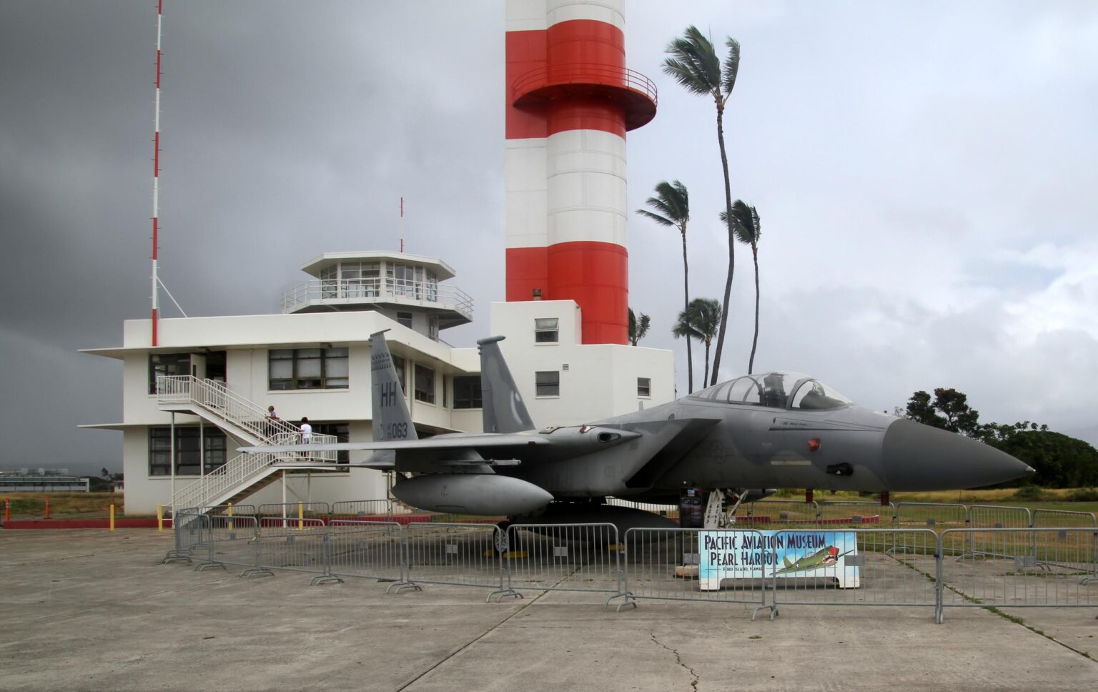 The red and white Ford Island Control Tower and the Operations Building at the Pearl Harbor Aviation Museum, with an F-15 on display in front
