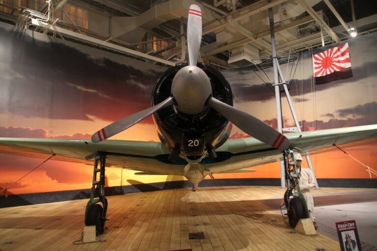 A Japanese Mitsubishi A6M2 Zero on a mock carrier deck in front of a sunset backdrop at the Pearl Harbor Aviation Museum