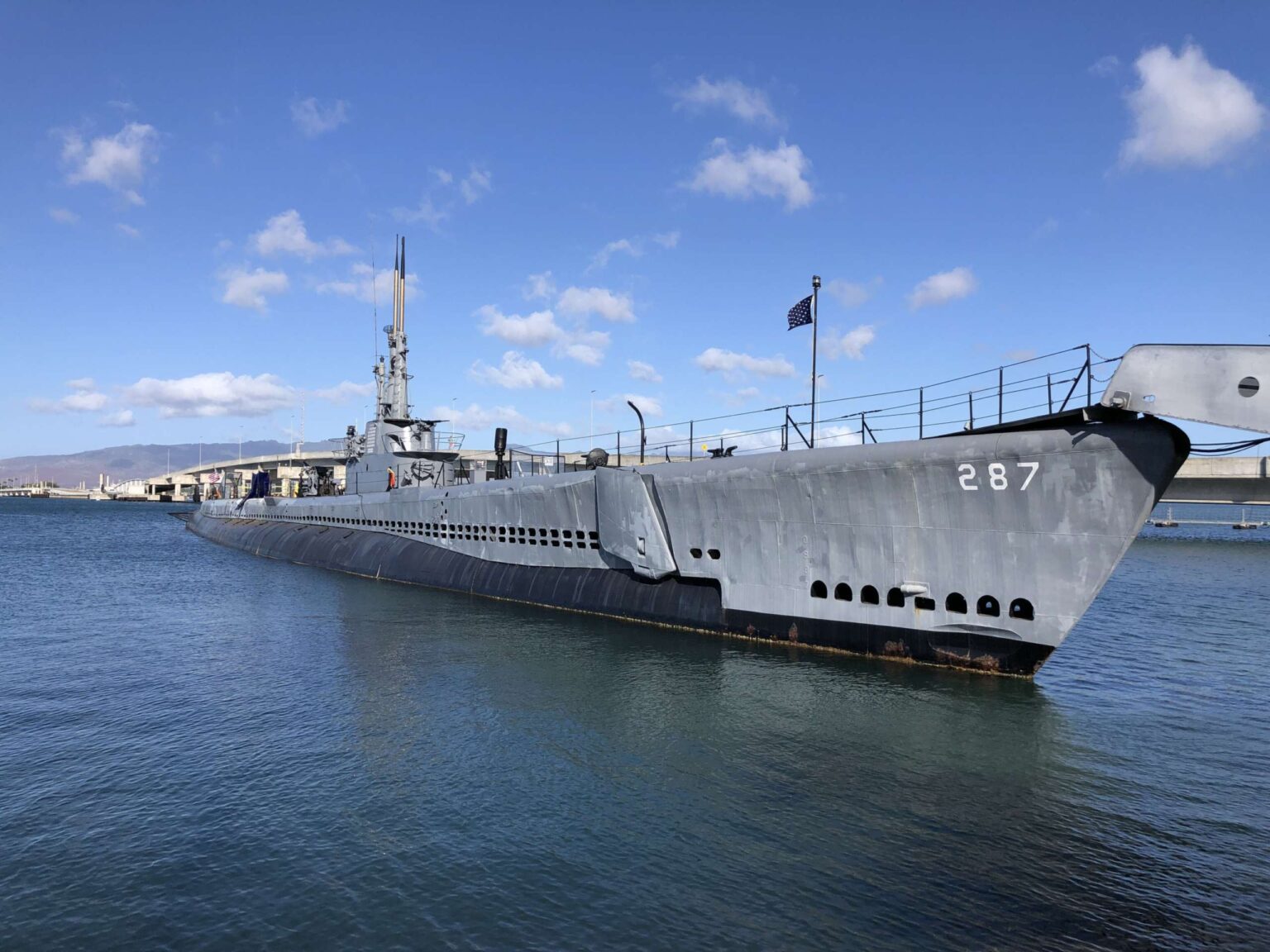 The USS Bowfin, a gray World War II submarine, moored at Pearl Harbor under a blue sky