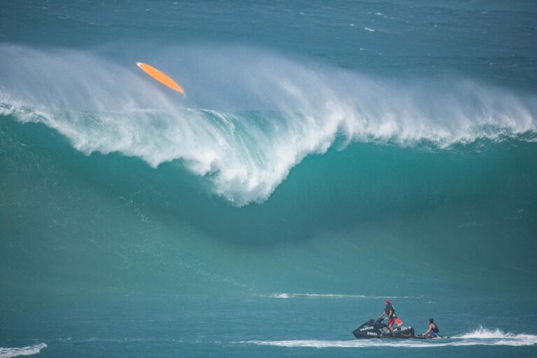 A huge wave breaking at Waimea Bay with a rescue jet ski in front of it during the 2016 Eddie Aikau Big Wave Invitational