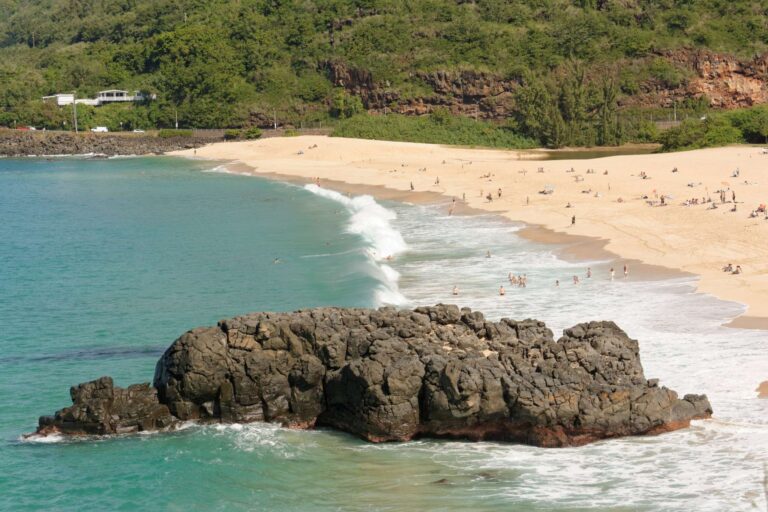 Waimea Bay beach on a calm day, with swimmers in the shore break and green cliffs behind